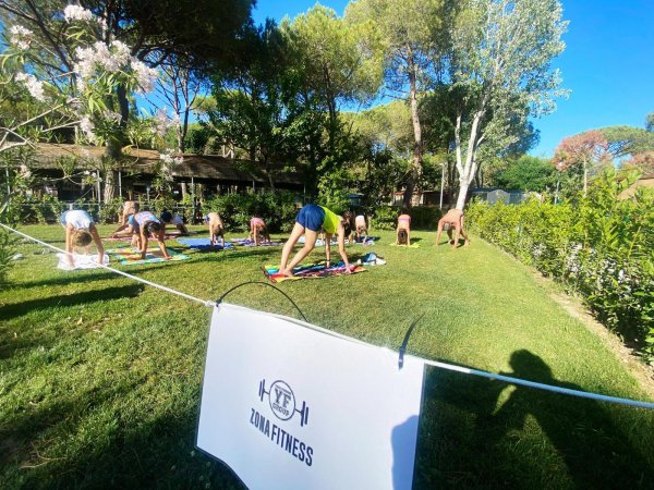 Gruppo di persone fa yoga su un prato verde in una zona fitness all'aperto, circondata da alberi.