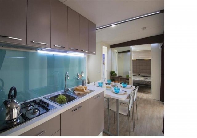 Cucina moderna con mobili beige, tavolo apparecchiato, finestra luminosa e pavimento in legno.