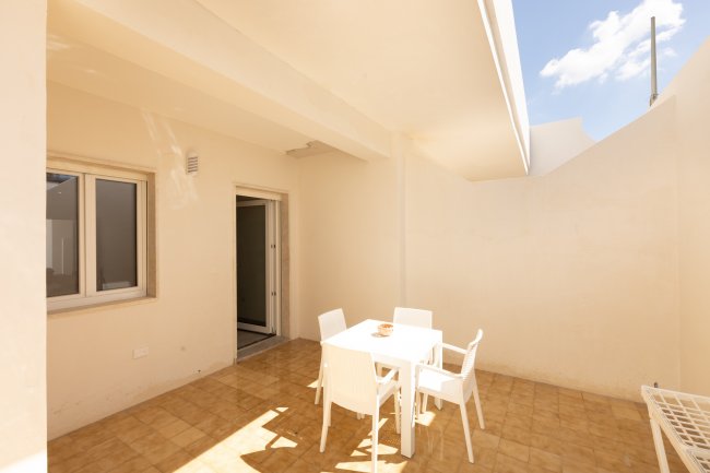Terrazza esterna con tavolo e sedie bianche.