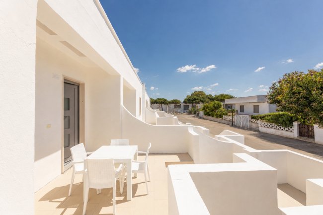 Terrazza bianca con tavolo e sedie, cielo blu limpido.