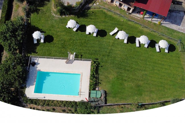 Vista dall'alto di una piscina con sdraio e ombrelloni su prato.