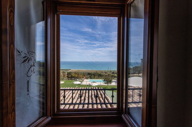 Vista mare da una finestra, piscine e giardino in basso.