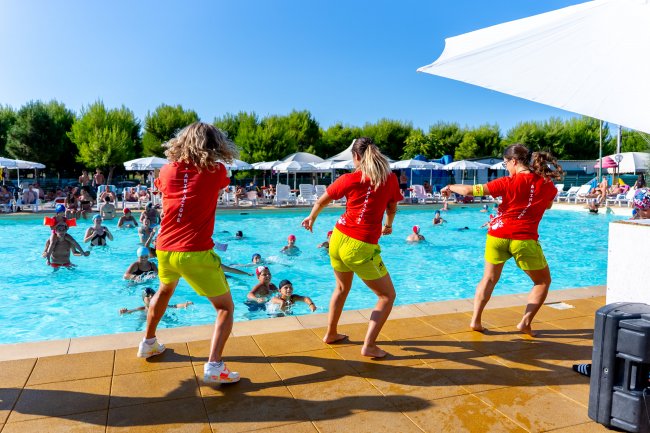 Tre istruttori fronte piscina animano il pubblico.