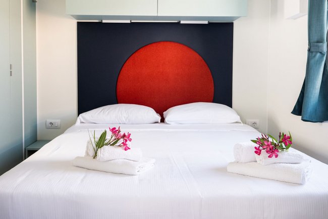 Letto matrimoniale con testiera rossa e fiori su asciugamani.