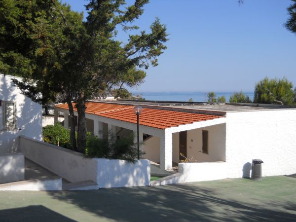 Edifici bianchi con tetto rosso, alberi, vista sul mare.