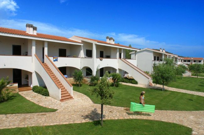 Edifici bianchi a due piani con scale esterne in un giardino ben curato.
