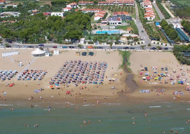Spiaggia affollata con ombrelloni e mare, dietro ci sono strutture e piscina.