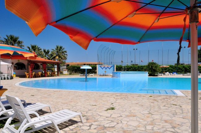 Piscina all'aperto con lettini e ombrelloni colorati su terrazza in pietra.