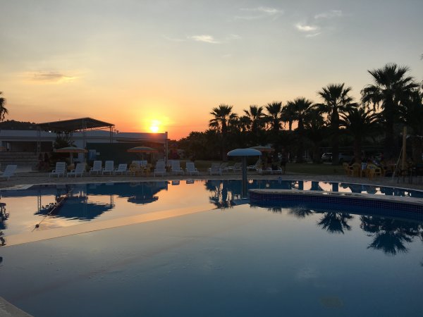Piscina all'aperto al tramonto con palme e sedie a sdraio sullo sfondo.