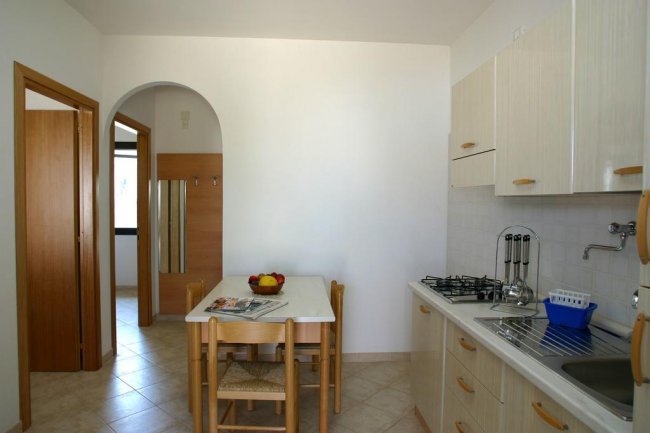 Una cucina semplice con tavolo di legno, sedie, lavandino e fornelli.