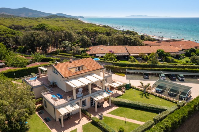 Una villa moderna con giardino vicino a una spiaggia e mare blu, vista dall'alto.