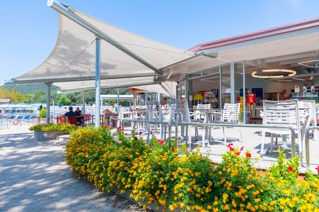 Terrazza di un bar all'aperto, con sedie bianche e fiori gialli, sotto un ampio tendone.