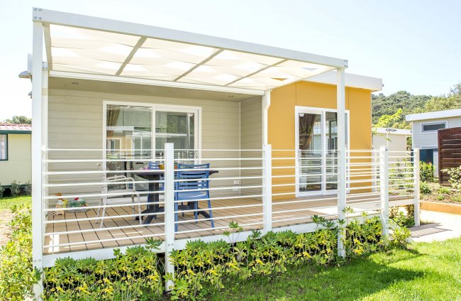 Una casetta con veranda coperta, mobili da esterno e giardino curato.