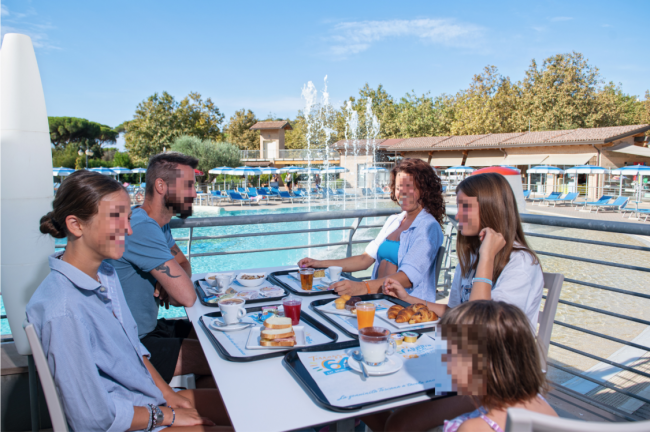 Famiglia a tavola vicino a una piscina, godendo di una colazione all'aperto.