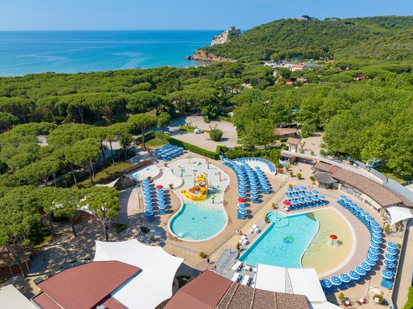 Complesso acquatico con piscine, ombrelloni blu e vista sul mare e colline verdi.