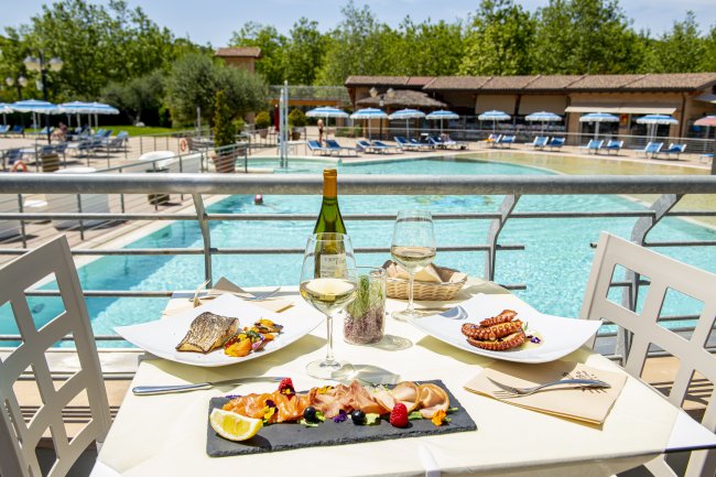 Tavolo con piatti gourmet e vino bianco accanto a una piscina.