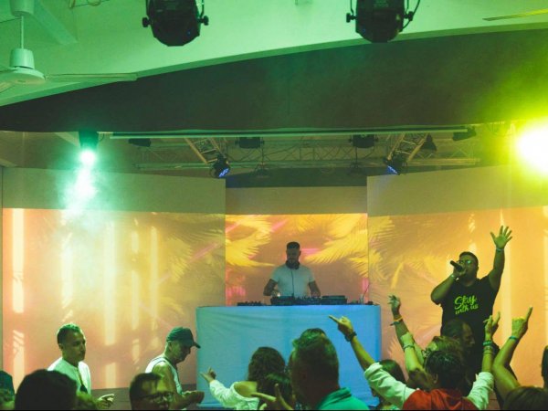 DJ su palco con pubblico in una discoteca illuminata.