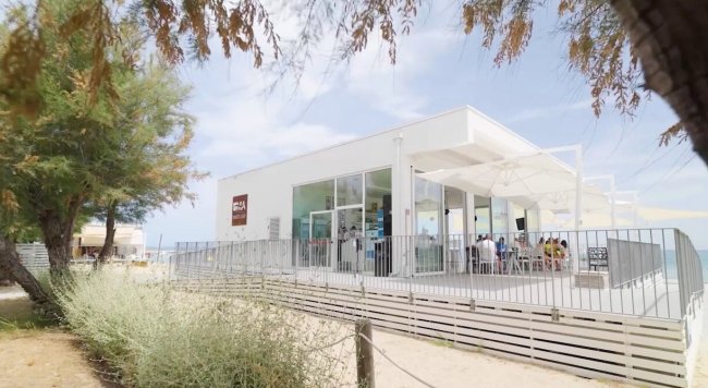 Un edificio moderno con terrazza sul lungomare, circondato da vegetazione.