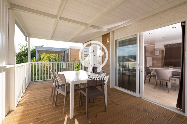 Terrazza coperta con tavolo e sedie in legno, vista su giardino e interni attraverso vetrata.