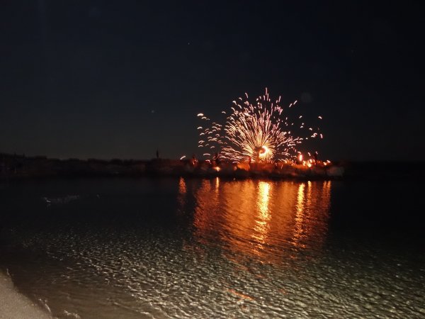 Fuochi d'artificio illuminano il cielo sopra l'acqua di notte.
