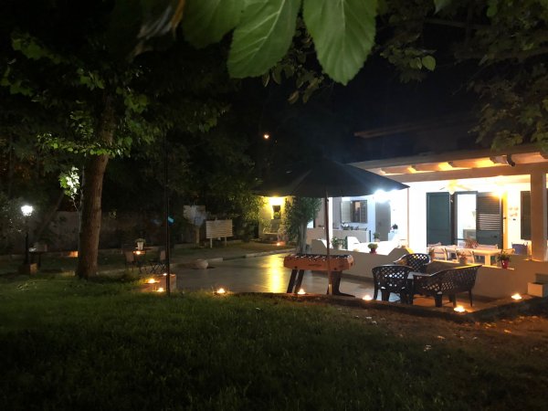 Spazio esterno notturno illuminato, con sedie e ombrellone.