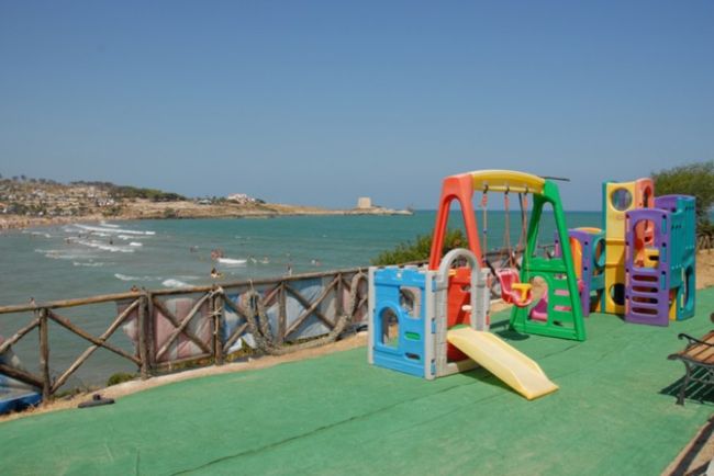 Area giochi colorata con vista mare, accanto a una staccionata in legno.