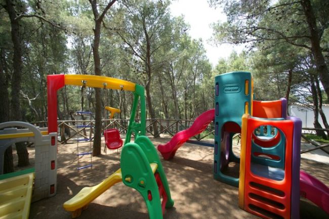 Un parco giochi con scivoli e altalene colorati tra alberi alti.