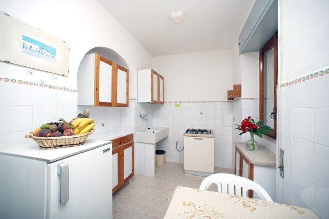 Cucina bianca con tavolo, cestino di frutta e vista sulla finestra.