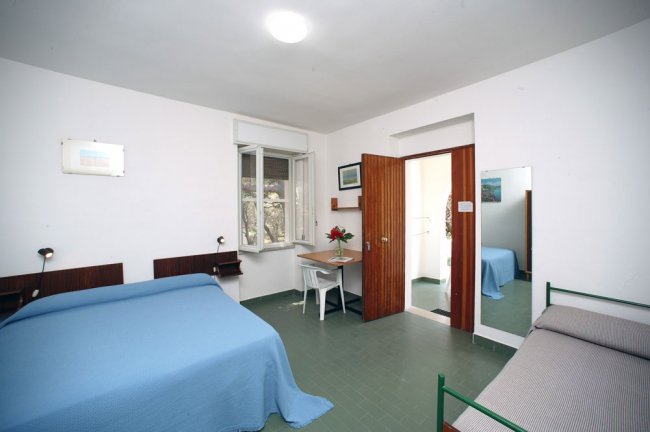 Camera con letto matrimoniale e singolo, scrivania sotto una finestra aperta.