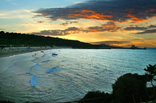 Spiaggia al tramonto con cielo rosso e mare mosso.