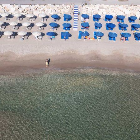 Spiaggia con ombrelloni blu e bianchi, persona vicino all'acqua.