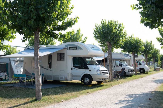 Una fila di camper parcheggiati vicino a una strada alberata.