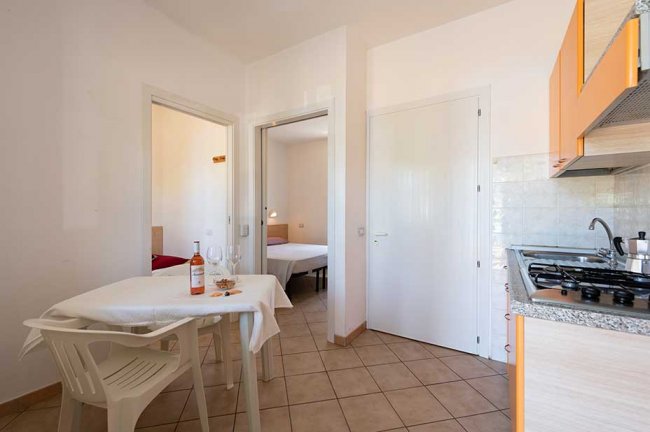 Cucina compatta con tavolo apparecchiato, due camere visibili sullo sfondo.