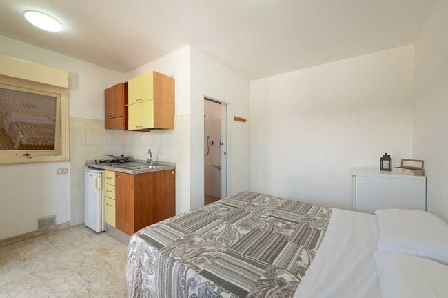 Stanza con letto matrimoniale, angolo cottura e bagno sullo sfondo.