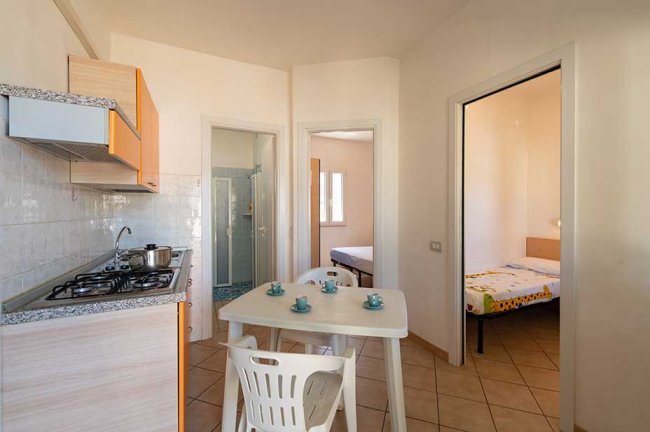 Cucina con tavolo e sedie, piano cottura, porte che conducono a camere da letto.