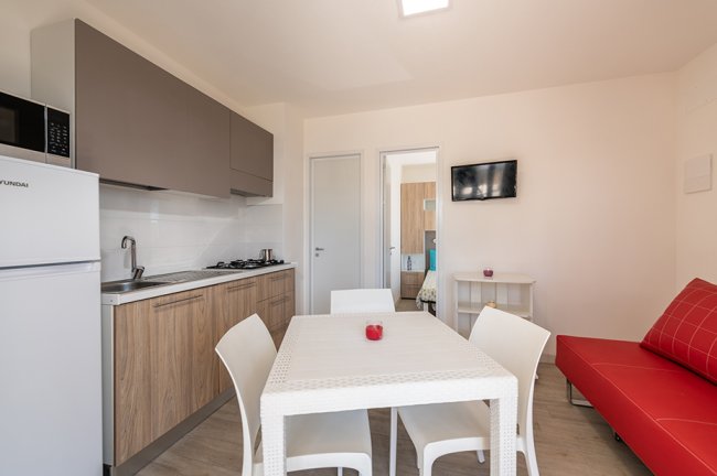Cucina moderna con tavolo, sedie e divano rosso.