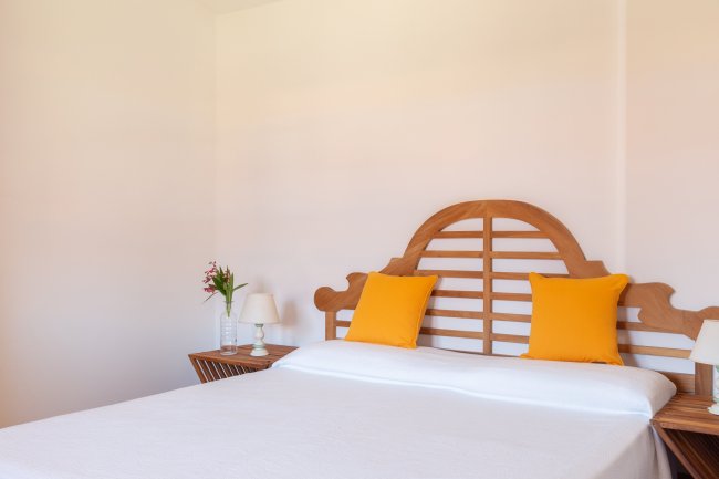 Camera da letto con letto matrimoniale, testiera in legno e cuscini gialli.