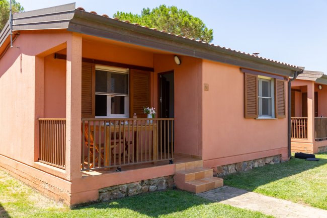 Bungalow rosa con veranda e finestre, circondato da prato curato.