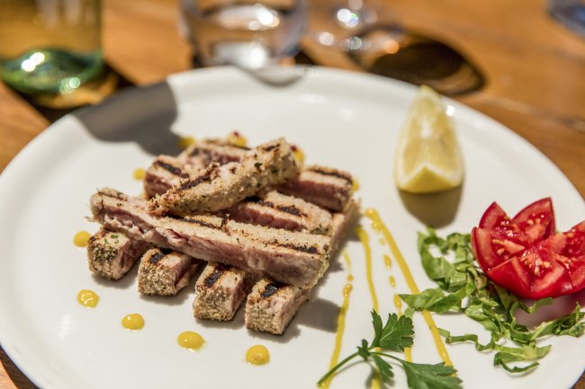 Piatti di pesce grigliato con limone, pomodori e foglie verdi su un piatto bianco.