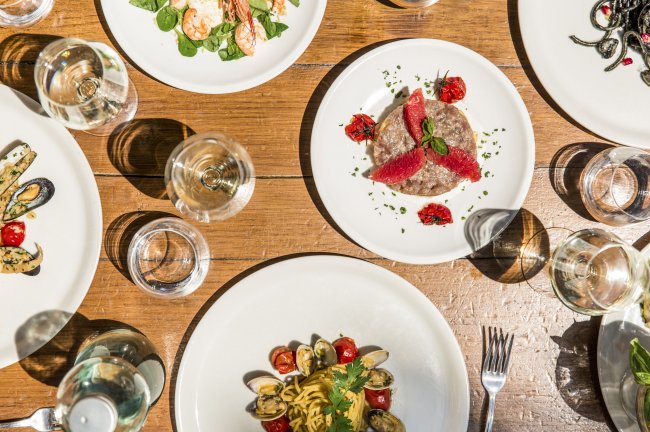 Tavola con vari piatti di cibo, tra cui pasta e frutti di mare, vista dall'alto.