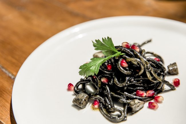 Spaghetti al nero di seppia con chicchi di melograno e guarniti con prezzemolo.