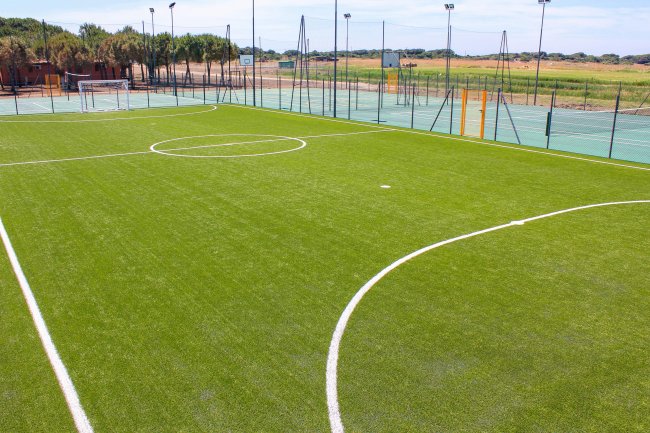Campo di calcio in erba sintetica con linee bianche e recinzione in lontananza.