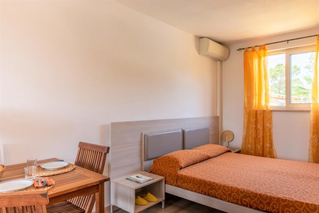 Una stanza luminosa con un letto arancione, tende arancioni, tavolo, e sedie in legno.