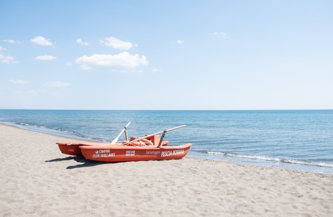 Una barca rossa sulla spiaggia di fronte al mare calmo, cielo azzurro.