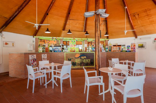 Locale con tavoli e sedie bianche, bar con insegna 