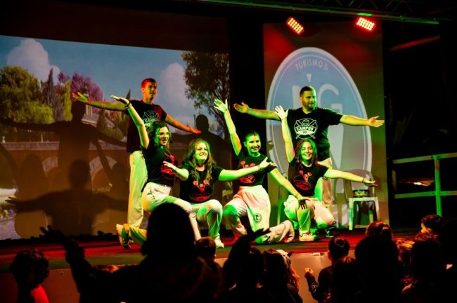Un gruppo di persone in posa su un palco, con luci colorate e pubblico in ombra.