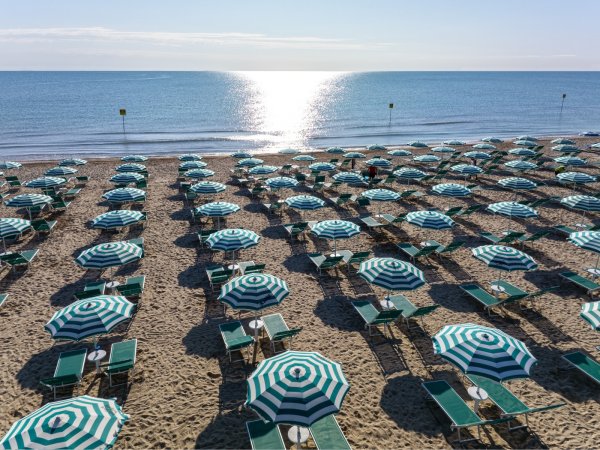 Spiaggia con fila di ombrelloni a righe verde e bianco e lettini di fronte al mare.
