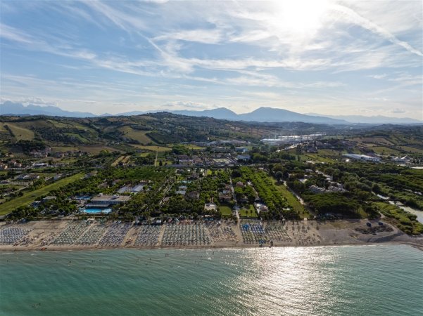 Panorama aereo di una costa con ombrelloni, resort e campagna collinare sullo sfondo.