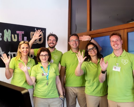 Sei persone in polo verde salutano festosamente davanti a una lavagna.