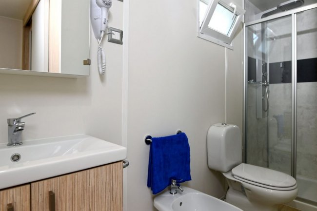 Bagno moderno con lavabo, bidet, WC, asciugacapelli e doccia con porta in vetro.